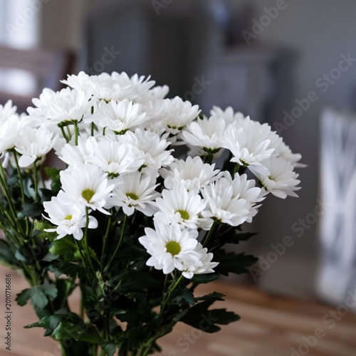 Bunch of White Flowers Placed on a Wooden Table With Green Leaves on a Neutra...