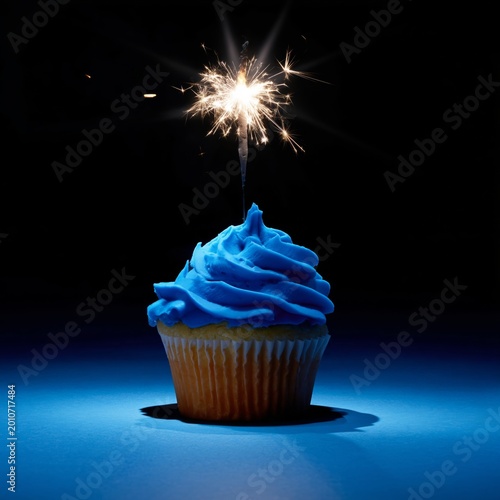 Cupcake With Blue Frosting Topped With a Sparkler on a Gray Background During...
