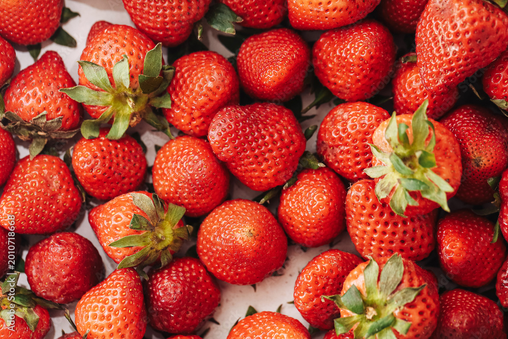 Naklejka premium Ripe strawberries fill the frame with red fruit and green leaves. Juicy seasonal harvest shows natural sweetness. Fresh berry texture creates vibrant food background. Market freshness fills image.