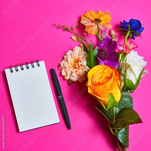 Bright Flowers and a Blank Notepad With a Pen on a Pink Background in a Creat...