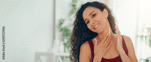 Foto A woman smiles while applying a skincare product to her neck and face in a bright room