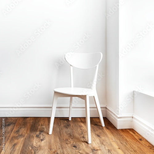White Chair Placed in Cozy Corner of Room With Wooden Floor and Plain Wall in...