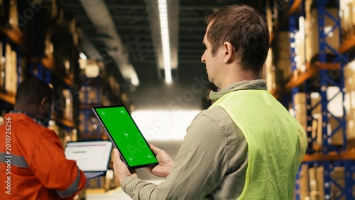 Foto Vertical mockup screen on tablet near warehouse staff in logistics hub, surrounded by parcels and cargo