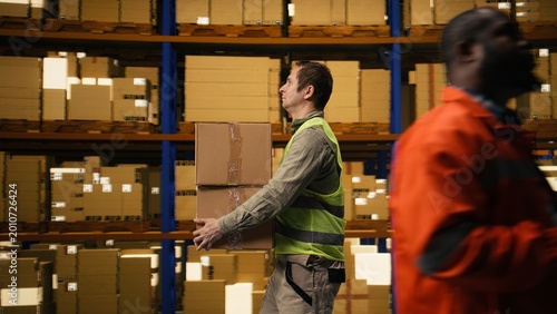 Canvas Print Male personnel sorting cardboard packages in logistics warehouse, connecting supply chain operations with import export cargo