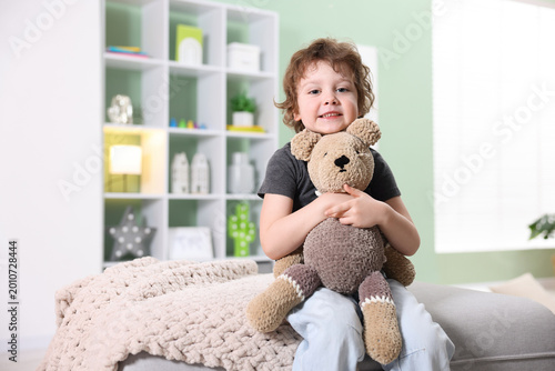 Tableau sur toile Smiling little boy hugging plush toy bear on pouf at home