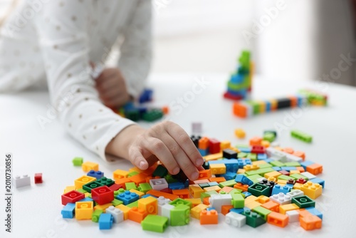 Little girl playing with colorful building blocks at white table indoors, closeup. Construction toy