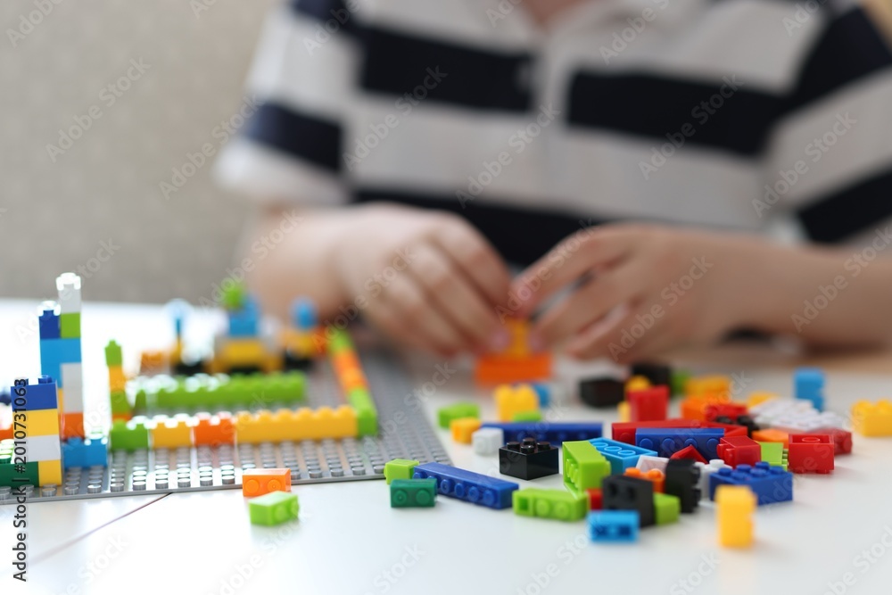 Fototapeta premium Construction toy. Little boy playing with building blocks at table indoors, closeup