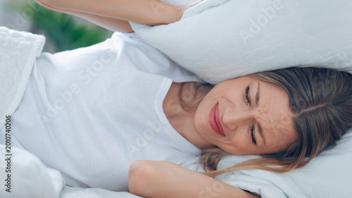 Obraz na płótnie A woman is in bed, covering her ears with pillows