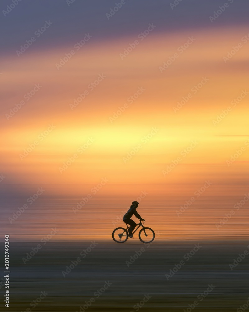 Obraz premium A lone cyclist silhouetted against a bright sunset, panning shot, horizontal motion blur, conceptual image of moving forward