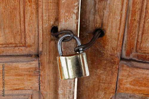 Detailed close up of an old scratched brass padlock and thick  wire securing weathered wooden doors. Eye-level view, selective focus. Concept of security and restriction