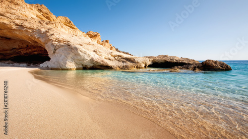 Rocky coastal cave with golden cliffs and clear turquoise water meeting sandy beach