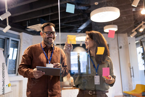 Business professionals collaborating on a project, brainstorming ideas with sticky notes on a glass board in an office
