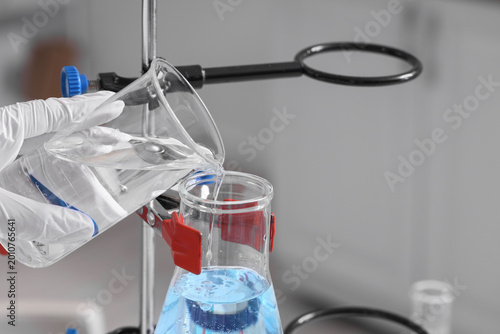 Female scientist's hand pouring water sample into flask in laboratory, closeup