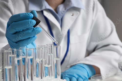 Female scientist dropping water sample into test tube in laboratory, closeup