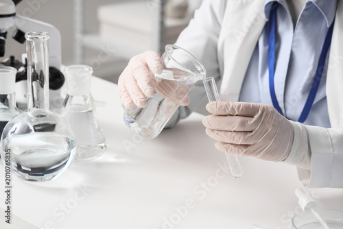 Female scientist pouring water sample from flask into test tube at table in l...