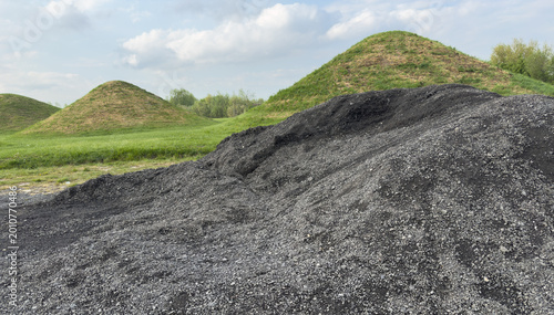 Fotografie Black coal slag pile with grassy hills in industrial landscape