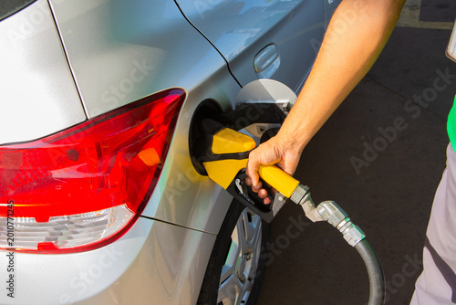 Close-up of person refueling a car with gasoline at a gas station, highlighting fuel consumption and transportation.