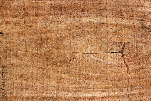 A detailed top-down view of a rough sawn timber surface showing natural brown wood grain, fibers, and organic patterns.