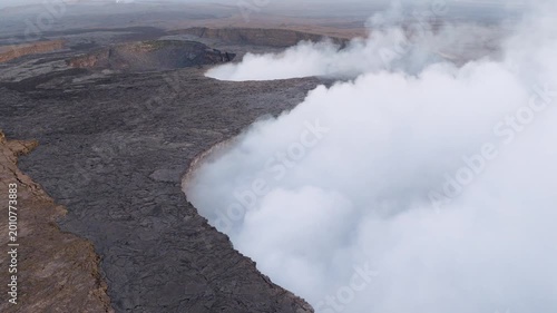 Aerial view of Erta Ale Volcano with thick white smoke rising from the dark volcanic crater and lava fields in Danakil Desert, Afar, Ethiopia.