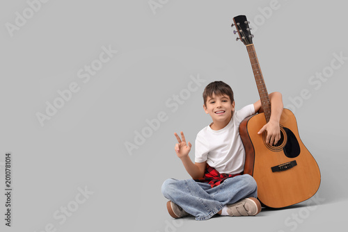 Cute boy with guitar sitting on light background