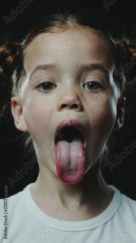 Young girl sticking out tongue against black background close up