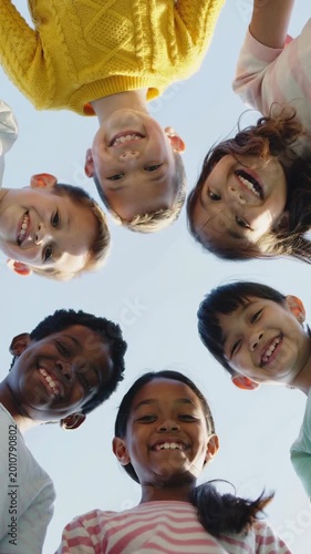 Diverse children looking down into camera lens against bright blue sky background low angle view