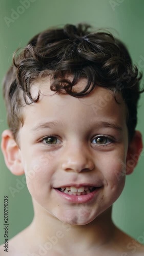 Young boy smiling with curly brown hair against green background close up shot