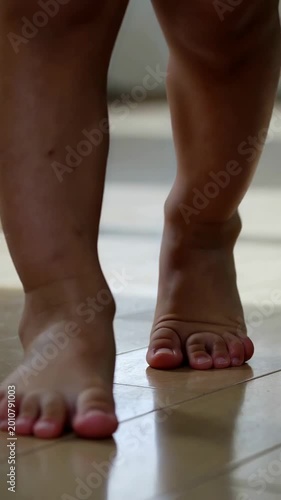 Toddler feet walking on light wooden floor indoors, close up shot of baby taking first steps