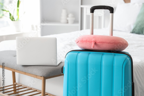 Suitcase with neck pillow in hotel room, closeup