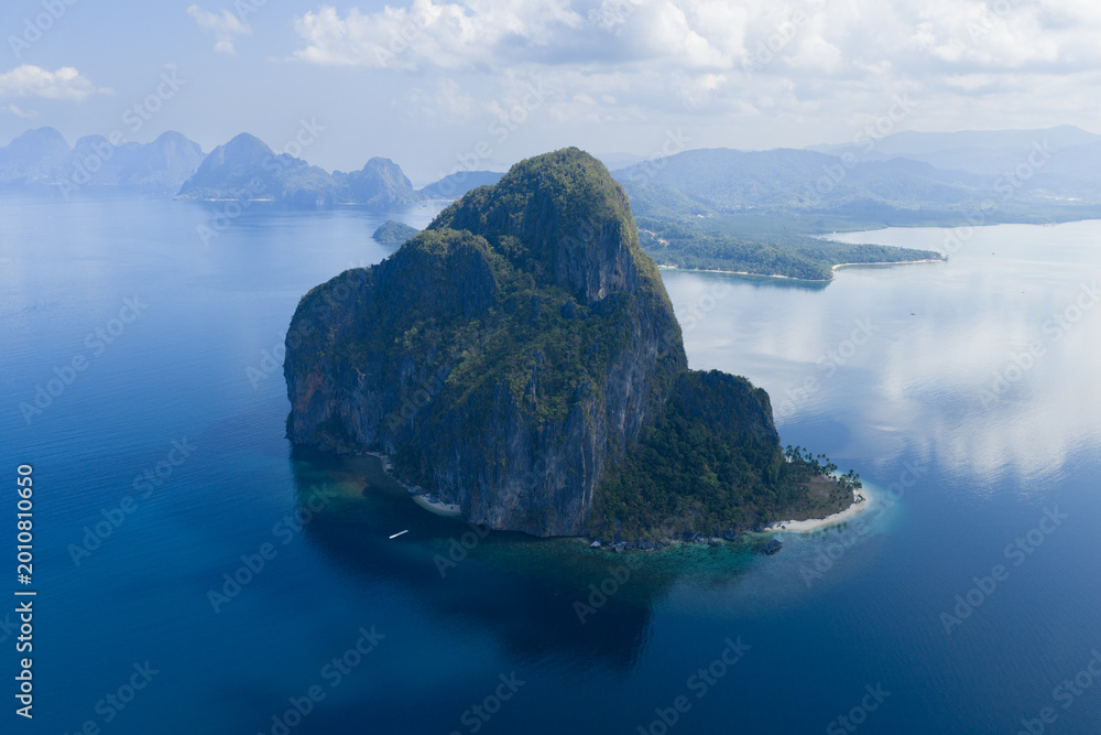 Obraz premium Glassy calm seas bathe the coastline of an idyllic limestone island in El Nido, Philippines. This area in Palawan is a popular vacation destination due to its coral reefs, beaches, and hidden lagoons.