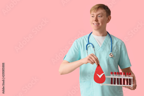 Male nurse with paper blood drop and test tubes on pink background