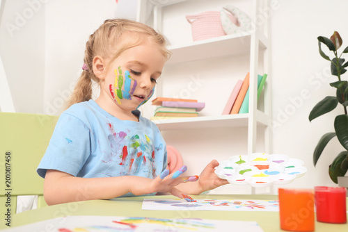 Cute little girl painting with her hand at table in bedroom