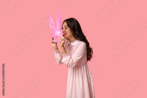 Beautiful young happy Asian woman in bunny mask on pink background