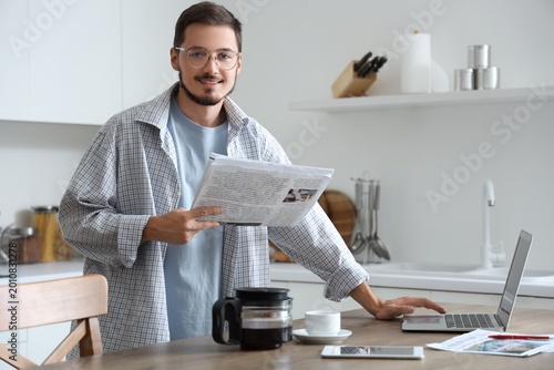 Foto Young man with newspaper using laptop in kitchen