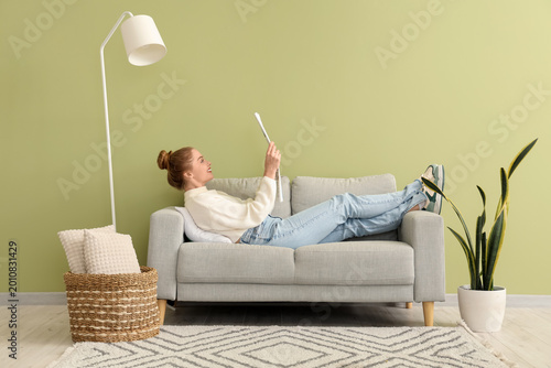 Quadro su tela Young woman reading newspaper on sofa at home