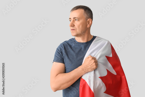 Mature man with flag of Canada on light background