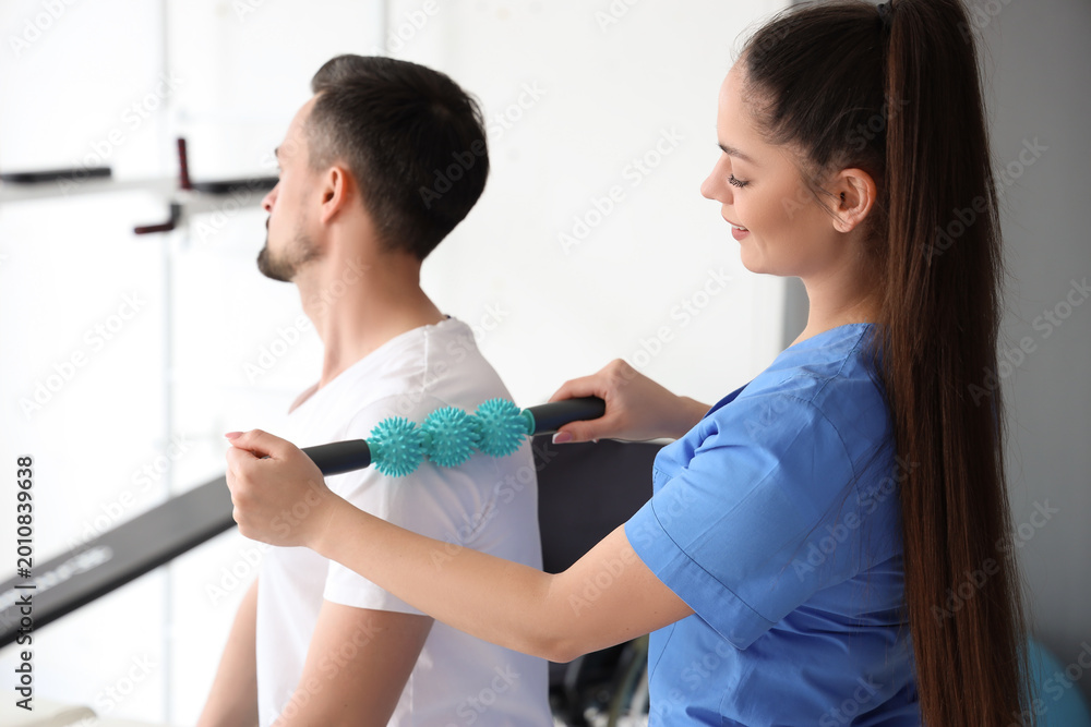 Fototapeta premium Female physiotherapist massaging young man in rehabilitation center