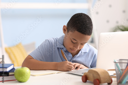 Little African-American boy studying computer sciences online in bedroom