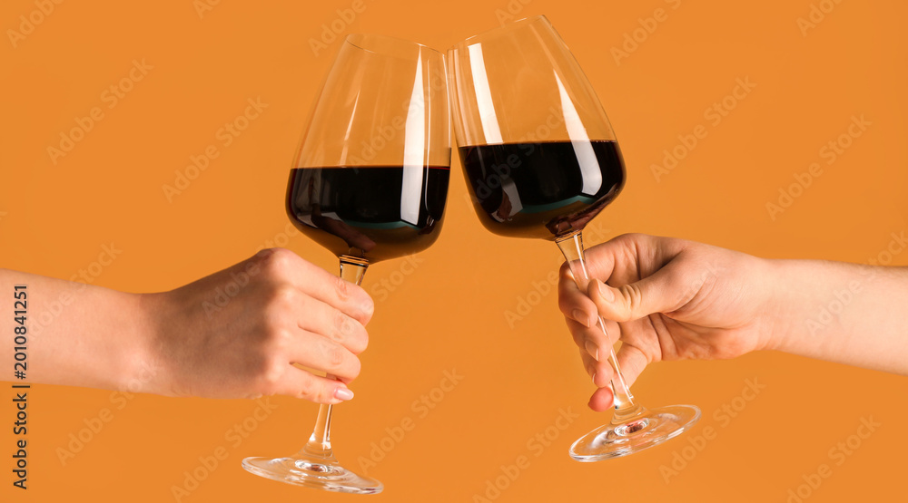 Fototapeta premium Female hands with glasses of red wine on orange background