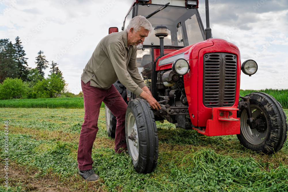 Obraz premium Man trying to repair a tractor on the field, using wrench, struggling 