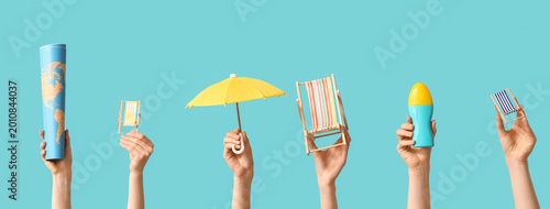 Fotografi Female hands holding mini deck chairs with umbrella, sunscreen and map on blue b