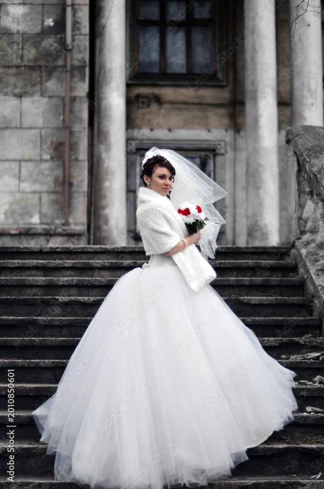 Obraz premium Beautiful bride standing on historic staircase in elegant wedding dress with dramatic romantic atmosphere and timeless European architecture. Charming bridal lifestyle portrait ideal for wedding