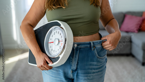 Woman holding scale showing weight loss with loose jeans