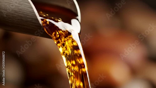 Slow Motion Macro Shot Of Viscous Amber Liquid Pouring From A Spout.