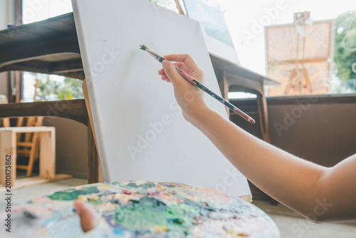 close-up art student's hand using watercolor paint brush painting on canvas doing some art projects on studio workshop