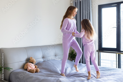 Two girls in matching pajamas jumping on a bed in a bright bedroom