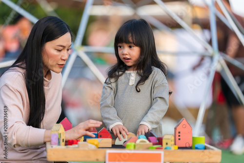 mother and preschool child girl playing with wooden toy block at outdoor