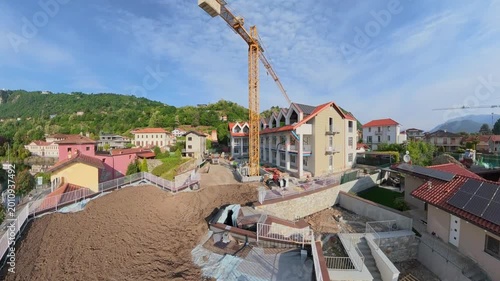Drone aerial view of a luxury modern house under construction overlooking Lake Orta, Italy, during sunrise. Cinematic panning shot featuring crane operations, residential development, construction equ