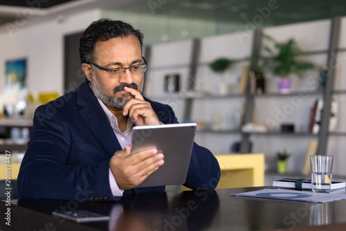 Obraz na plátne Thoughtful businessman sits in coworking office, reviewing report on digital tab