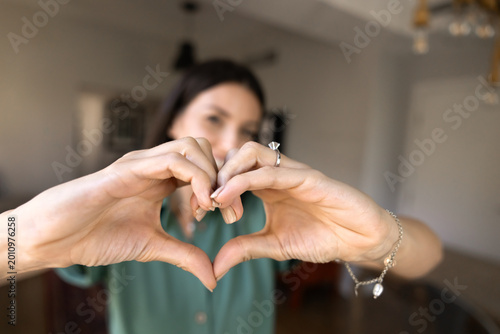 Schilderij op canvas Close up view adult woman shaping heart symbol with her hands, standing alone in living room at home